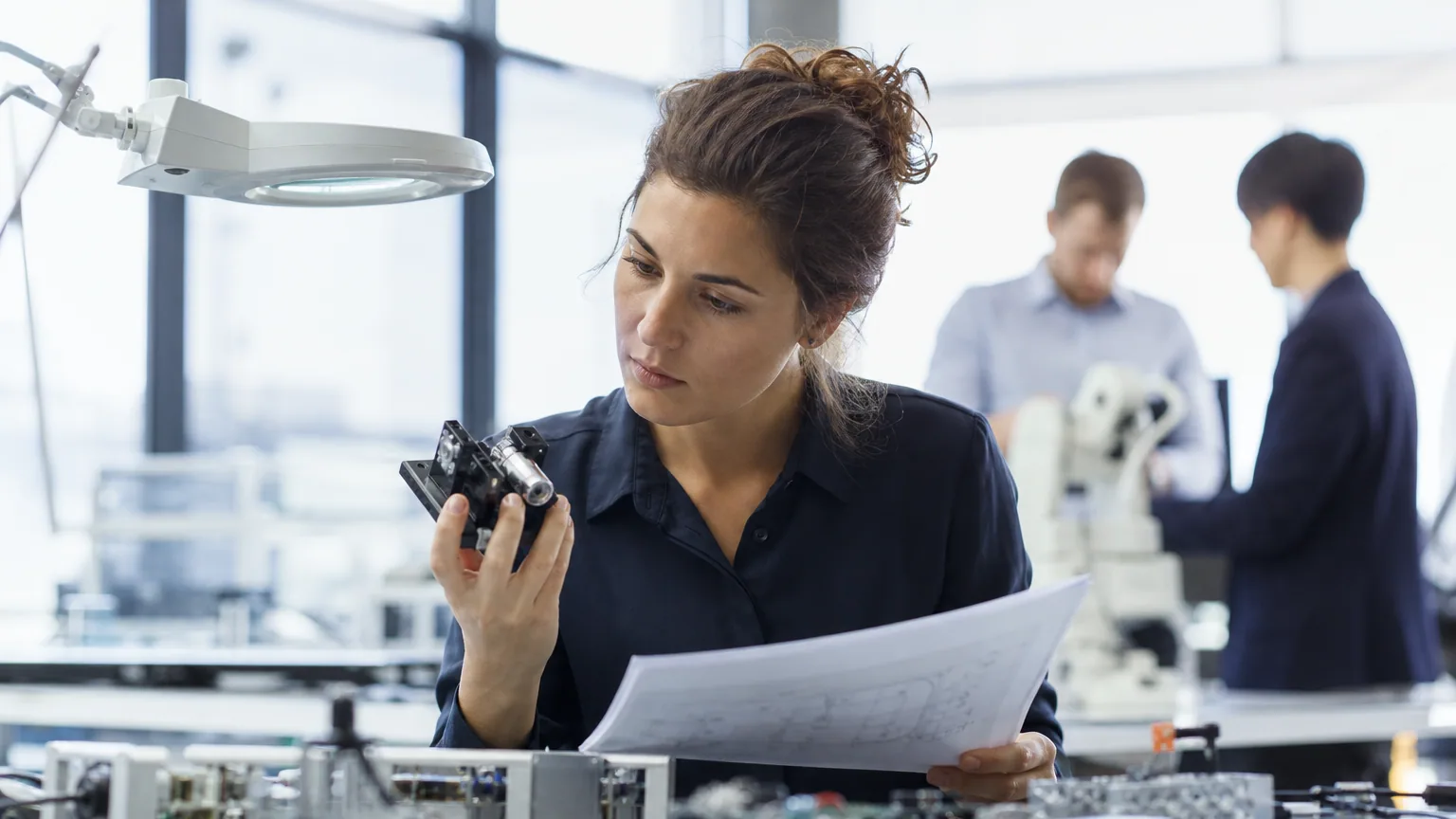Une ingénieure examine un prototype dans un laboratoire de deep tech avec des documents techniques