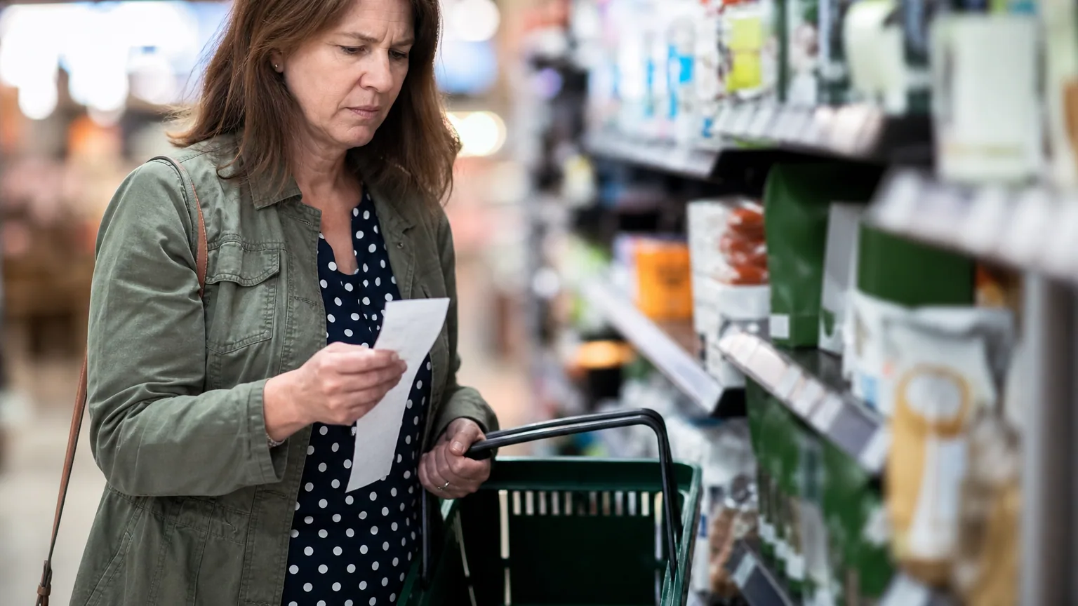 Une personne inquiète tient un ticket de caisse dans un supermarché face à des prix en hausse.
