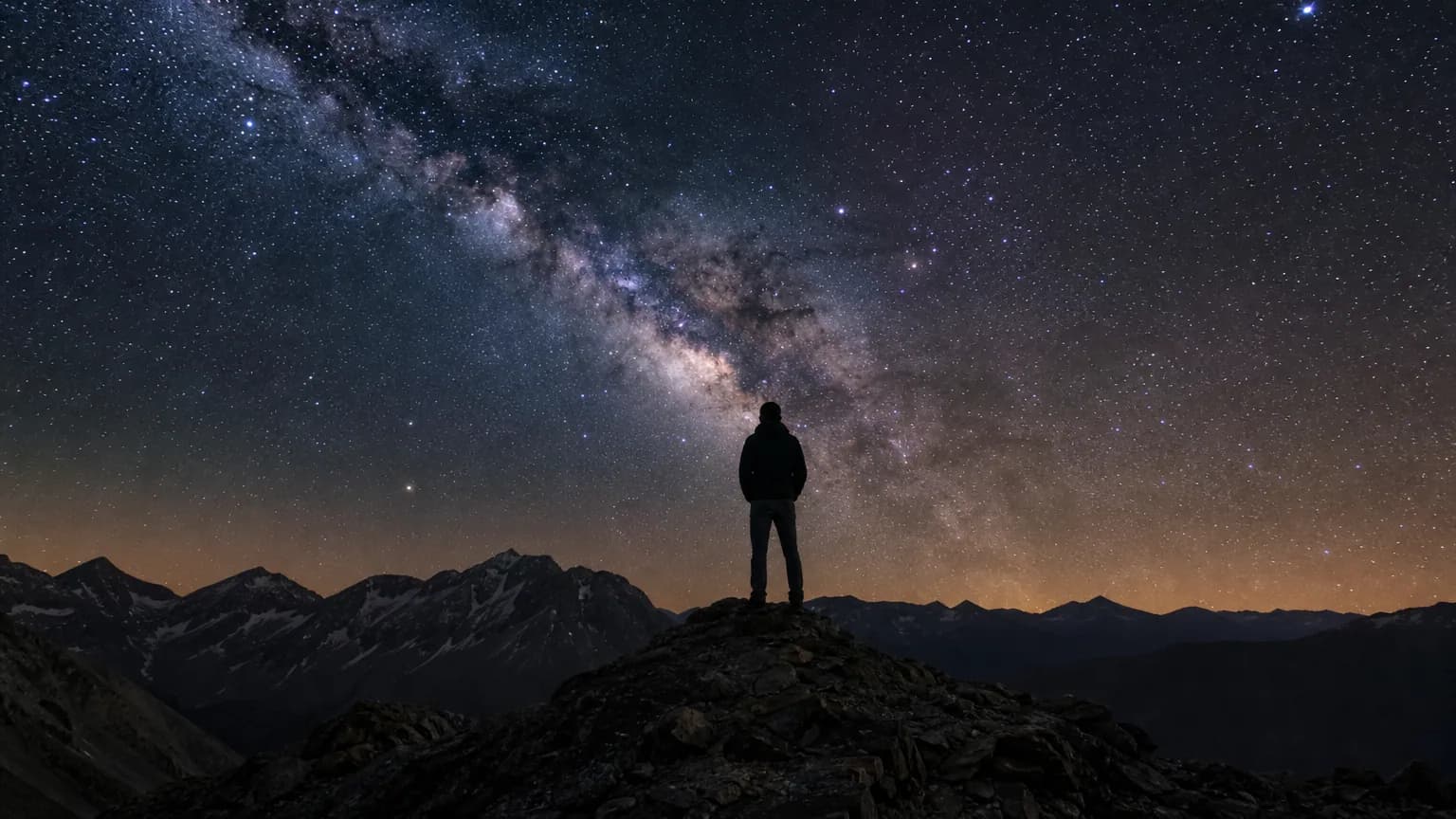 Une personne observant l'arc lumineux de la Voie lactée dans un ciel nocturne étoilé depuis une montagne