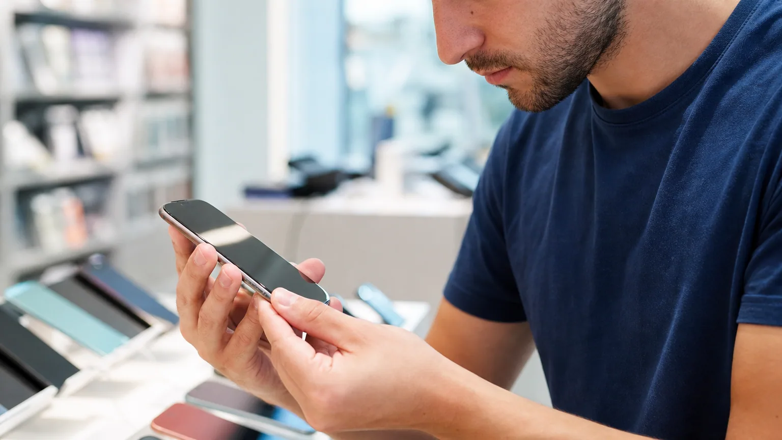 Une personne examine attentivement l'écran d'un smartphone reconditionné en magasin
