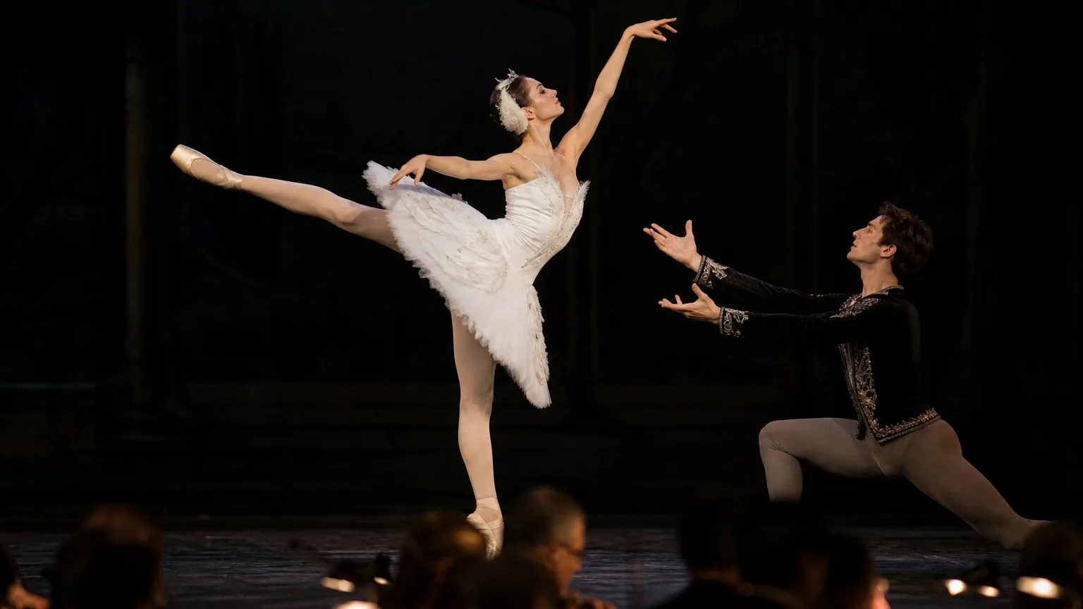 Une danseuse en tutu blanc en pleine arabesque sous un projecteur, partenaire tendant la main vers elle
