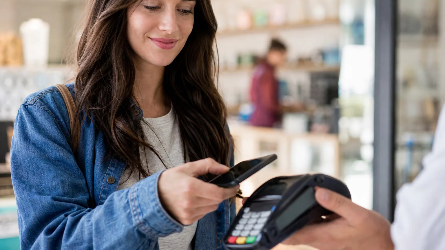 Une personne approche son smartphone d'un terminal de paiement sans contact en magasin